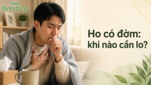 Người đàn ông quấn chăn, ôm ngực và che miệng khi ho trong phòng khách, bên cạnh dòng chữ “Ho có đờm: khi nào cần lo?” và logo Dược Bình Đông.