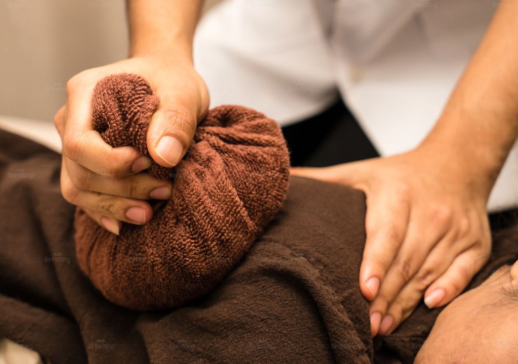 Người phụ nữ đang chườm nóng vùng bụng bằng túi thảo dược để giảm khó chịu và thư giãn cơ thể