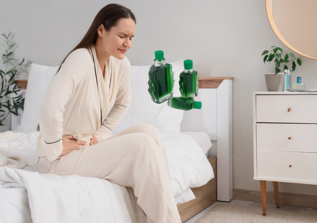 Phụ nữ ôm bụng dưới vì đau bụng kinh, cạnh chai dầu gió dùng để giảm đau tạm thời