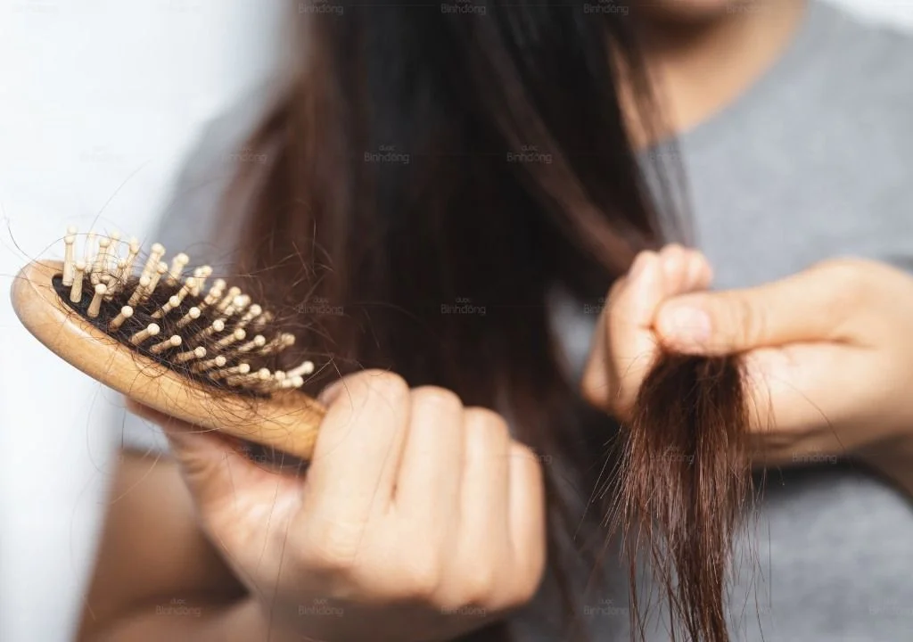 Người phụ nữ chải tóc và thấy tóc rụng nhiều trên lược.