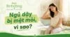 Người phụ nữ ngồi ở mép giường, một tay xoa trán, vẻ mặt uể oải. Dòng chữ nổi bật: “Ngủ dậy bị mệt mỏi, vì sao?