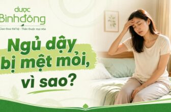 Người phụ nữ ngồi ở mép giường, một tay xoa trán, vẻ mặt uể oải. Dòng chữ nổi bật: “Ngủ dậy bị mệt mỏi, vì sao?